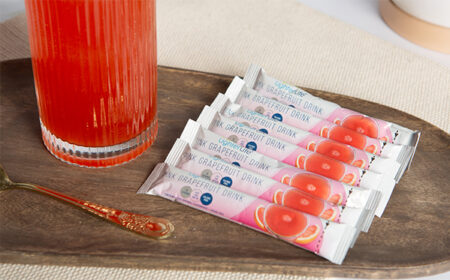 7 pink grapefruit drink mix sachets next to a glass of drink