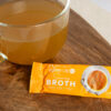 savoury broth in a glass mug next to sachet